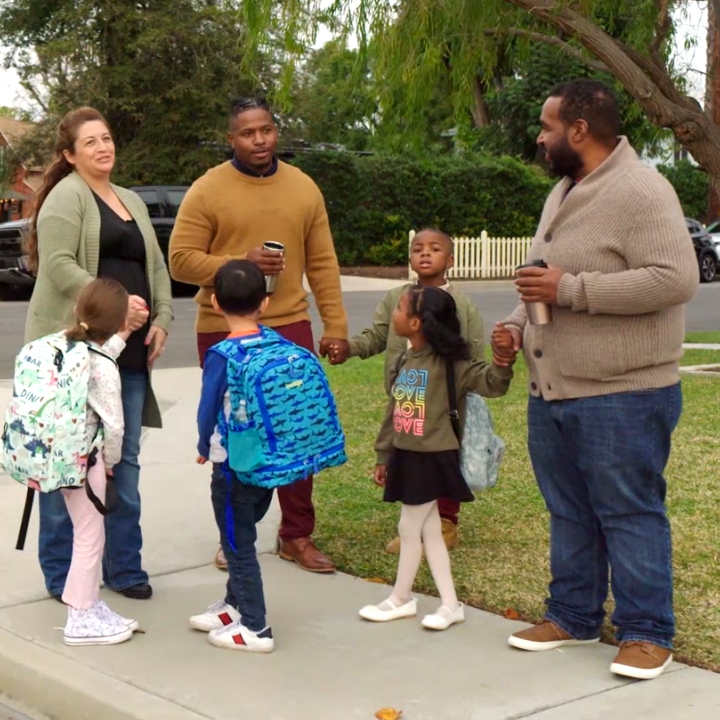 Parents stand with their children at the bus stop, discussing what happens when term life insurance ends.