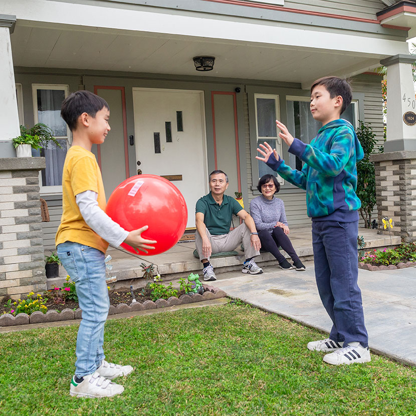 Two boys play with a ball outside while their grandparents smile knowing they have TruStage whole life insurance