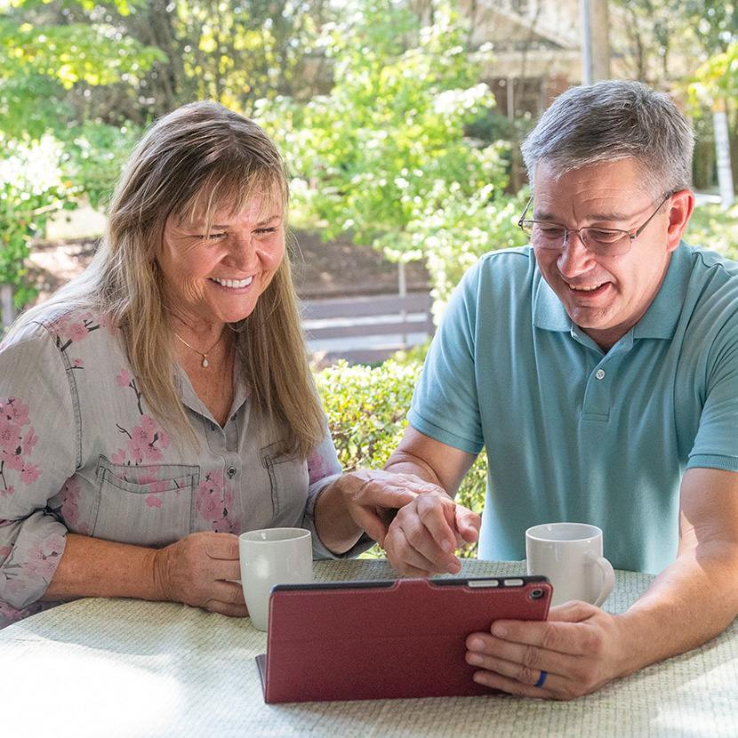 A man and a woman, both seated and with a tablet, are discussing their retirement portfolio.